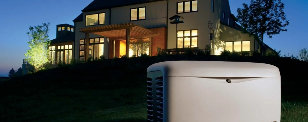 Photo of house in background with kohler generator in foreground. It is dusk and the lights are on in the house