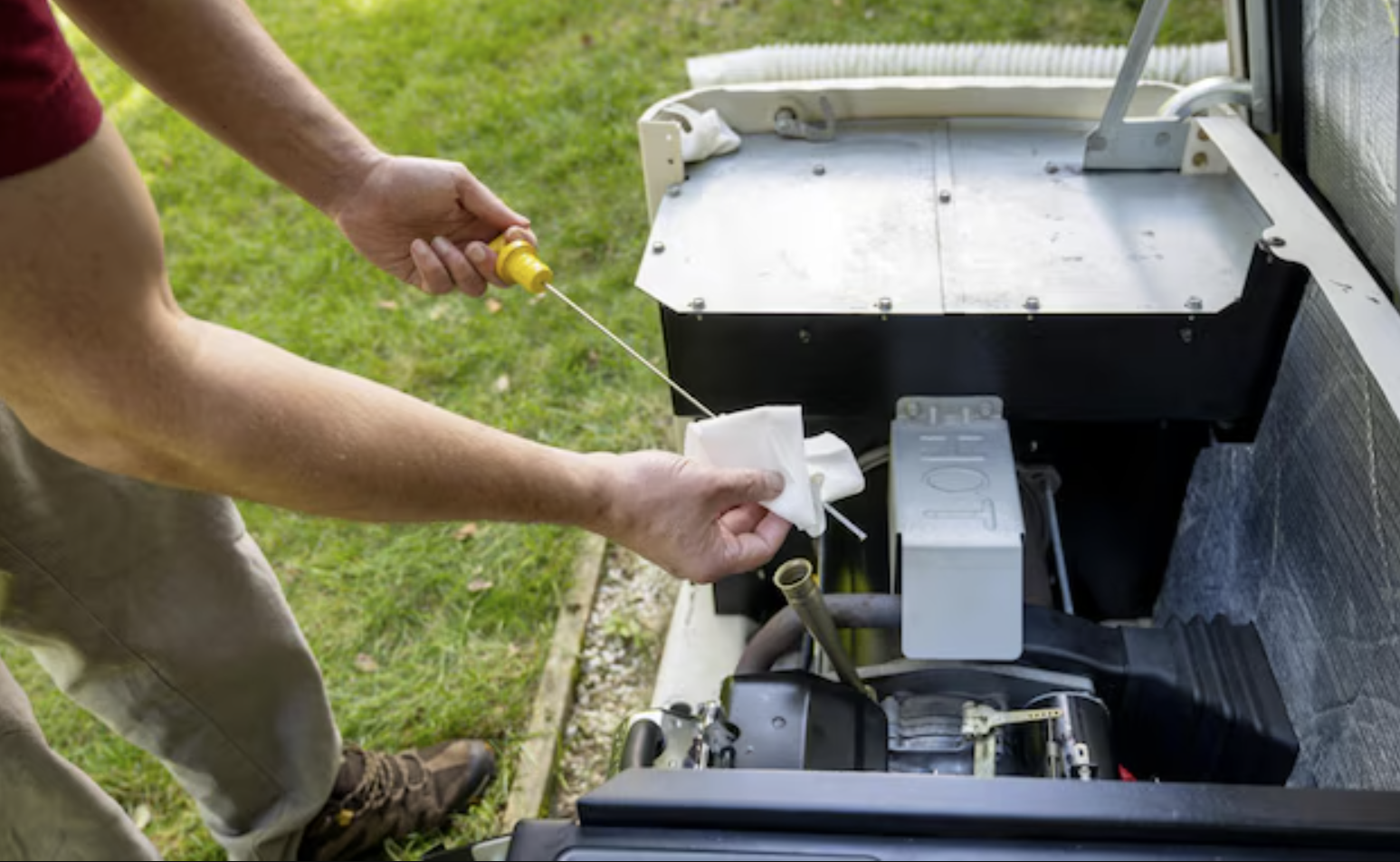 photo of a man checking the dipstick in a generator engine. The image is close cropped so only the man's arms and left leg are visible to the left of the frame, and the generator engine appears large in the right half of the frame.